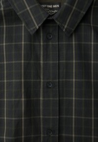 Tmavě zelená kostkovaná košile vyrobená z látky, s klasickým límečkem, předním zapínáním na knoflíky a kontrastními světle béžovými mřížkovými linkami.