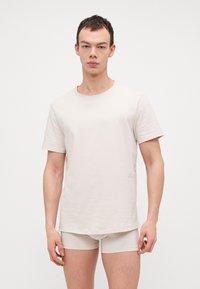 Helle beige T-Shirt mit rundem Ausschnitt und kurzen Ärmeln, aus einem weichen Stoff gefertigt, kombiniert mit passenden hellbeigen Shorts.