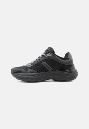 Baskets épaisses noir et gris foncé avec le logo "GUESS" sur le côté, semelle texturée et fermeture à lacets, présentées en vue de profil.