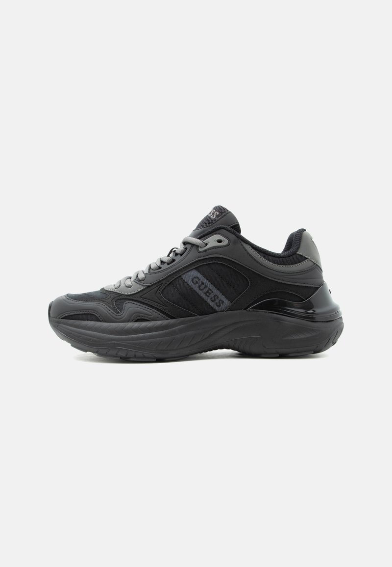 Baskets épaisses noir et gris foncé avec le logo "GUESS" sur le côté, semelle texturée et fermeture à lacets, présentées en vue de profil.