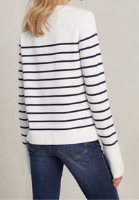 Vit tröja med marina horisontella randar, rund halsringning och långa ärmar, matchad med mörkblå jeans. Mjuk stickad textur, avslappnad design.