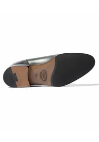 Suela de zapato de cuero negro con un acabado suave y un agarre de goma. Presenta una etiqueta de plantilla en color marrón y adornos metálicos decorativos. Textura antideslizante.