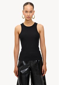 Top de tirantes negro con cuello redondo y diseño sin mangas, combinado con pantalones negros brillantes que presentan una textura de cocodrilo.