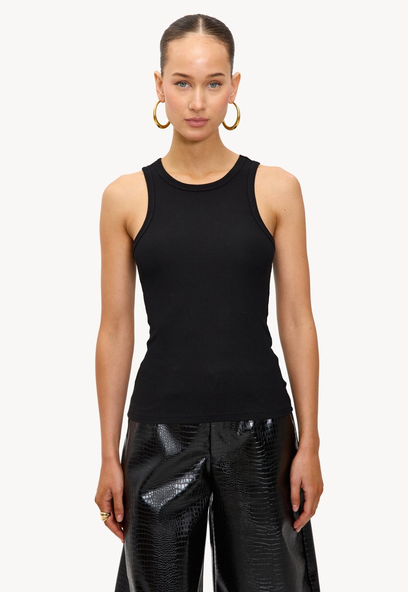 Top de tirantes negro con cuello redondo y diseño sin mangas, combinado con pantalones negros brillantes que presentan una textura de cocodrilo.