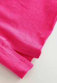 Rosa Baumwollstoff mit glatter Textur, der kontrastierende Nähte und ein umgeschlagenes Saumdetail aufweist.