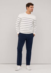 Suéter blanco con rayas azul marino, escote redondo y mangas ajustadas, combinado con pantalones azul marino y zapatillas blancas. Diseño sencillo y aspecto casual.