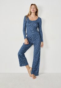 Conjunto de pijama de dos piezas en tela azul oscuro con un patrón floral blanco; la parte superior de manga larga presenta un escote en forma de barco y botones; pantalones acampanados.