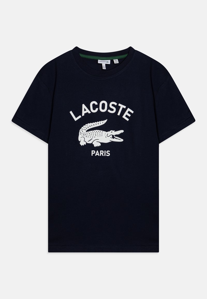 Tumed puuvillane T-särk, millel on valge krokodilli logo ja paksus kirjas "LACOSTE PARIS" tekst, mis asub graafika kohal keskel. Lühikesed varrukad.