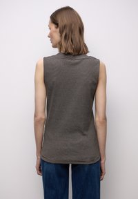 Szary, bezrękawnik z dzianiny z poziomymi paskami; miękka faktura, zaokrąglony dekolt i lekko dłuższy tył. Połączony z ciemnoniebieskimi dżinsami.