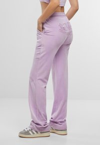 Lila velours broek met een relaxte pasvorm, voorzien van zijzakken en "Von Dutch" borduursel op de achterkant. Gepaard met grijze en witte sneakers.