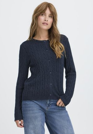 Námornícky modrý kardigan s pletenou štruktúrou, okrúhly výstrih, dlhé rukávy, zapínanie na gombíky vpredu, textúrovaná tkanina, priliehavý pás, skombinovaný s džínsami.