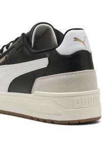 Black and white leather sneaker with a textured surface, suede heel, cream midsole, and gold Puma logo on the back.