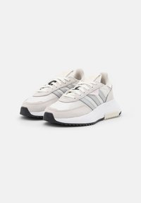 Ljusbeige sneakers med överdel av mocka och tyg, tre grå ränder på sidan, vit mellansula och svart gummisula.