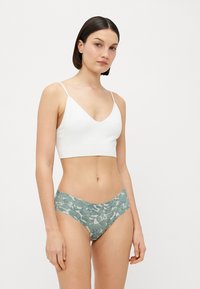 Fehér bralette V-nyakú kialakítással és vékony pántokkal, zöld mintázatú bugyival, amely katonai álcázás mintát mutat.