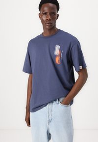 Navy blue cotton t-shirt with short sleeves, featuring a graphic print on the left chest area. Loose fit and classic crew neckline.
