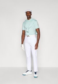 Polo azul claro, calças brancas e sapatos de golfe brancos com detalhes em azul. Uma boina branca e uma luva completam o conjunto.