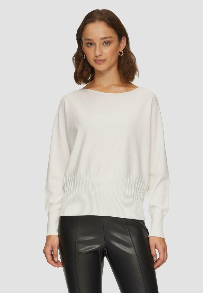 Pull en tricot blanc avec un encolure large et une taille côtelée, associé à un legging en cuir synthétique noir. Texture douce et coupe décontractée.