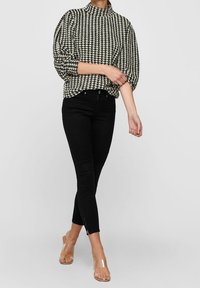 Pull-over à motif pied-de-poule noir et blanc avec un col haut, associé à un jean skinny noir et des sandales transparentes avec des fermetures éclair à la cheville.