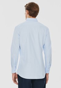 Jasnoniebieska koszula z długim rękawem, z kołnierzykiem zapinanym na guziki, z pojedynczym karczkiem na plecach oraz z mankietami zapinanymi na guziki. Gładki materiał z delikatną strukturą.