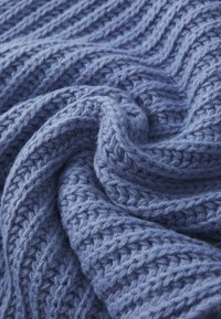 Coperta lavorata a maglia in morbida e testurizzata lana blu con un motivo a zig-zag, caratterizzata da una trama allentata e fibre visibili.