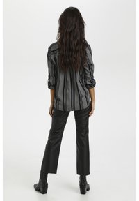 Zwart en grijs gestreepte blouse met opgerolde mouwen, gecombineerd met hoge zwarte leren broeken en zwarte enkellaarsjes.