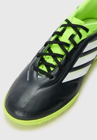 Chaussure de football noire et vert néon avec une finition texturée, dotée de lacets noirs, de trois bandes blanches et d'un design de bout rond.