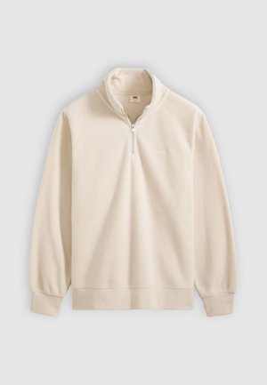 Polarowa bluza w jasnym beżu z wysokim kołnierzem, zamkiem na pół, ściągaczami na rękawach i subtelnym haftem logo na piersi.