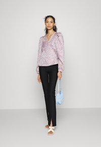 Blusa de padrão floral com mangas bufantes, combinada com calças pretas com fendas laterais. Acessórios com uma bolsa azul clara e sandálias brancas.