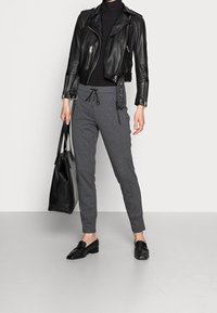 Svart skinnmotorcykeljacka över en tajt svart polotröja, kombinerad med gråa avsmalnande mjukisbyxor och svarta loafers. Accessoarer inkluderar en svart tote-väska.