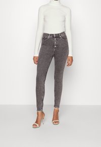 Hubené džíny ze světlého šedého denimu s vysokým pasem, pěti kapsami a zapínáním na knoflík, spárované s přiléhavým bílým rolákem a tělovými lodičkami.