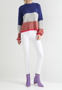 Strickpullover mit blauen, grauen und korallenfarbenen Streifen, mit rundem Halsausschnitt und geripptem Saum. Kombiniert mit weißen Skinny Jeans und lila Knöchelstiefeln.