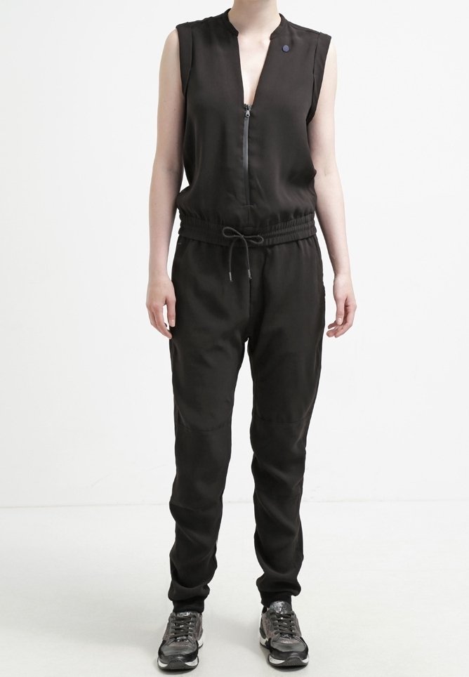 Czarny bezrękawnik z zamkiem błyskawicznym z przodu, elastycznym paskiem w talii i zwężającymi się nogawkami. Wykonany z gładkiego materiału, z małym dekoracyjnym guzikiem.