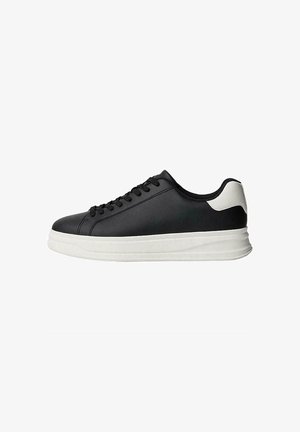 Zwarte sneaker met een gladleren bovenwerk, ronde neus, witte rubberen zool en contrasterende witte hakaccent. Zes eyelets voor veters.
