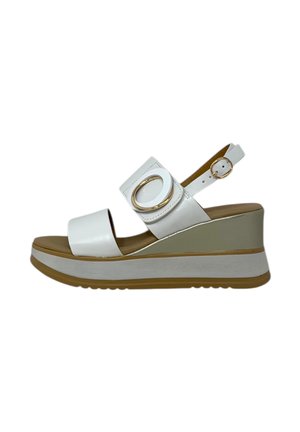Sandali wedge bianchi con una fascia frontale e una fascia alla caviglia regolabile, dotati di un accento metallico rotondo e una suola con texture.