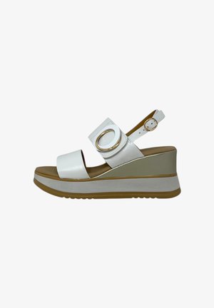 Sandali wedge bianchi con una fascia frontale e una fascia alla caviglia regolabile, dotati di un accento metallico rotondo e una suola con texture.