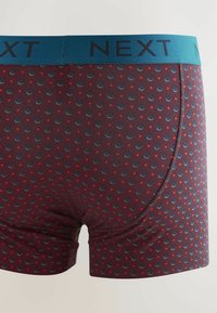 Boxeri scurți burgundii cu un brâu elastic albastru. Prezintă un model cu buline de culoare albastră închisă și roșie. Textura țesăturii este netedă.