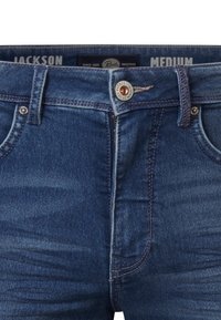 Niebieskie dżinsy o dopasowanym kroju, z metalowym guzikiem i zamkiem błyskawicznym, kieszeniami z przodu oraz kontrastowymi szwami.