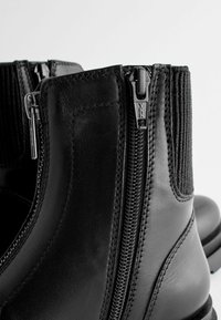 Svarta läderankelboots med ribbat textilpanel. Har en blixtlåsstängning och en slät yta med kontrasterande sömmar.