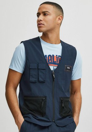 Navy blue vest with a zip front, two chest pockets, and two mesh-lined front pockets. Made from lightweight fabric with a smooth texture.