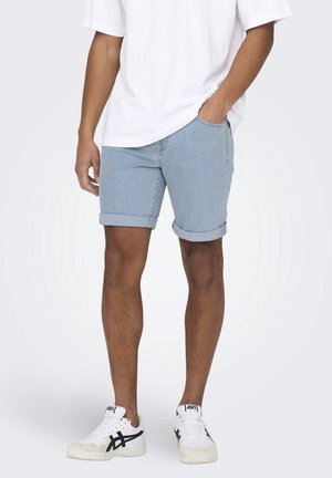 Shorts de denim en azul claro, con puños enrollados y diseño de cinco bolsillos. Combinados con una camiseta blanca holgada y zapatillas blancas con acentos negros.