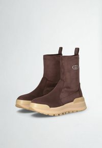 Stivaletti in suede marrone con suola spessa beige, caratterizzati da dettagli con logo e linguette per facilitare l'indossamento, texture liscia e design elegante.