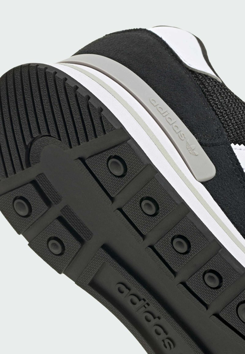 Black and white Adidas sneaker sole with textured grip and logo embossed on the bottom and side of the heel area.