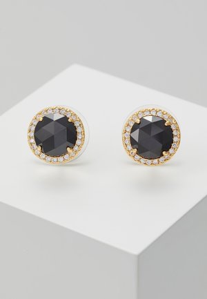 Okrągłe złote kolczyki na sztyft z dużymi czarnymi fasetowanymi kamieniami otoczonymi małymi przezroczystymi kryształkami, prezentowane na białej powierzchni.