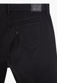 Černé denimové kalhoty s kapsou na zadní straně a vyšitým vzorem a šedou etiketou Levi Strauss na pase. Hladká textura.