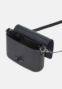 Černá kožená crossbody taška s cylindrickým vrškem, plochým obdélníkovým dnem, stříbrným kováním a zavíráním na cvok; hladká textura po celé ploše.