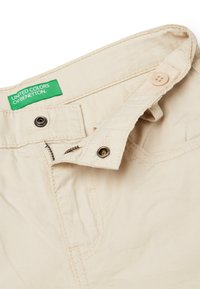 Béžové bavlněné kalhoty s knoflíkovým a zipovým zapínáním, se zelenou etikou označenou "United Colors of Benetton" a detailním prošíváním.