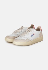 Sneaker bianche con accenti in suede beige, suole in gomma, design perforato e tassello rosso sul tallone. Presentano chiusura con lacci e una patch con logo laterale.