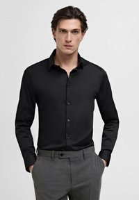 Black long-sleeve button-up shirt with a classic collar, smooth texture, and front button closure, paired with gray trousers.