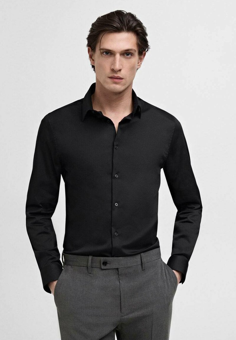Black long-sleeve button-up shirt with a classic collar, smooth texture, and front button closure, paired with gray trousers.