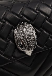 Czarna pikowana skórzana torebka z metalowym broszką w kształcie sowy w kolorze srebrnym, zdobioną kryształowymi akcentami oraz szczegółowym wzorem przypominającym pióra.